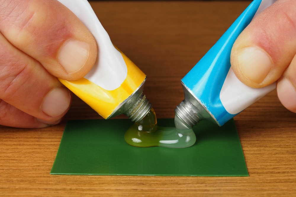 hand holding two tubes of epoxy adhesive for mixing